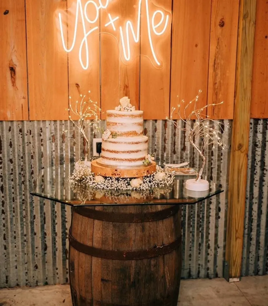 Wedding cake on a barrel table in front of a lit neon sign