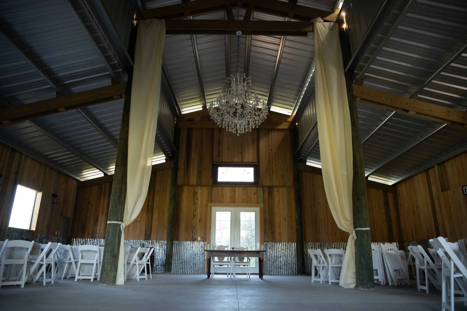 Inside the barn with ivory drapes and a chandelier hanging from the beams