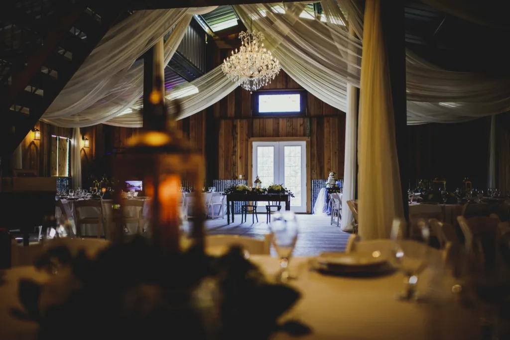 Candlelit reception tables inside the barn under draped fabric and a chandelier