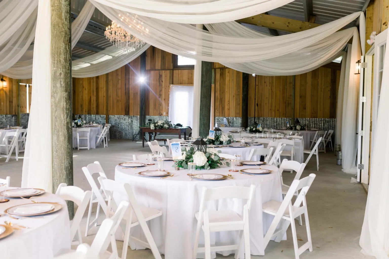 Barn reception with round tables, white linens and fabric draped from the rafters