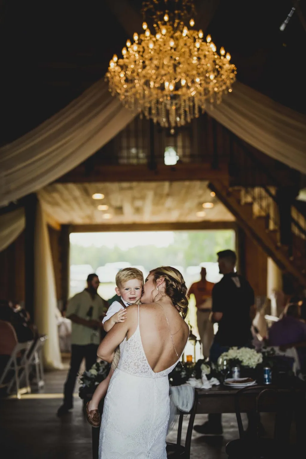 Bride embracing a guest in the barn beneath a gold chandelier