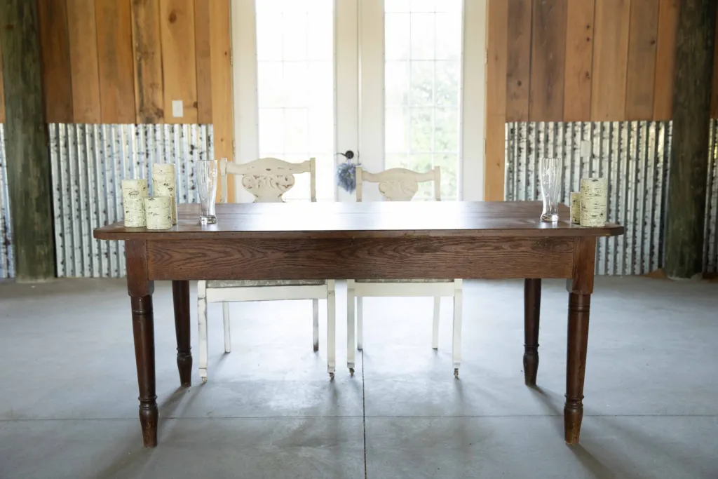 Wooden farm table and white chairs set inside the barn doors