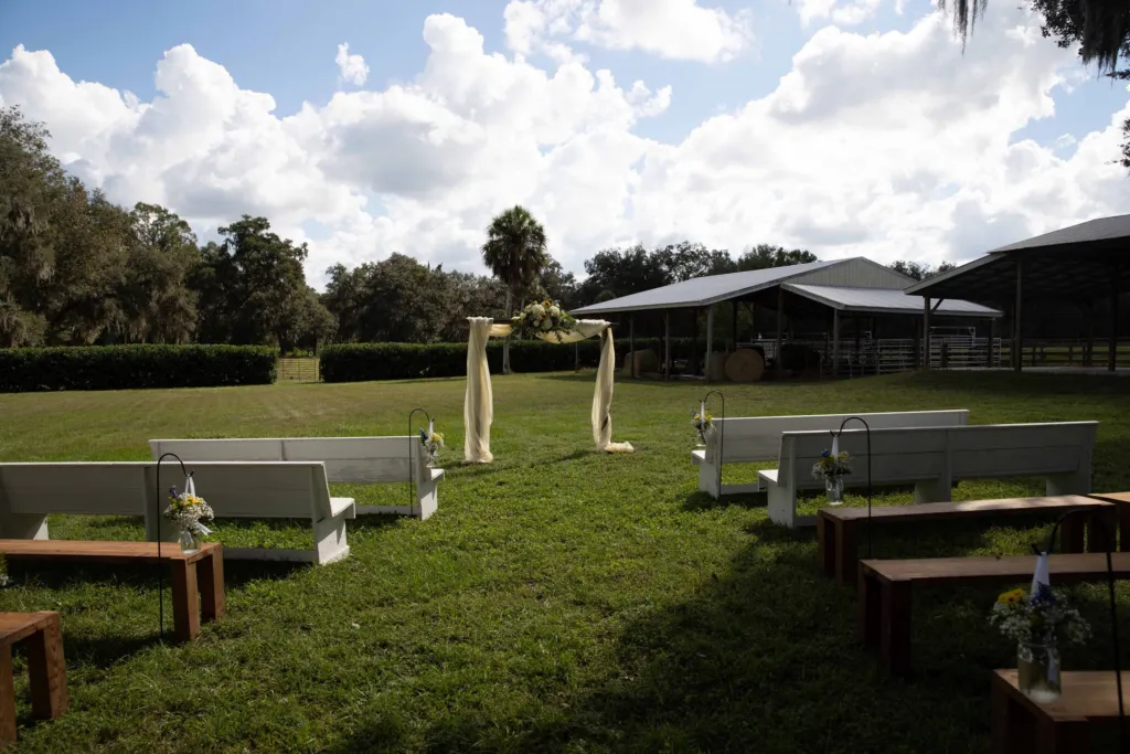 Wooden benches set on the lawn facing a draped ceremony arbor