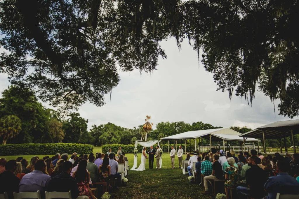 Guests watch an outdoor ceremony under live oaks draped in Spanish moss