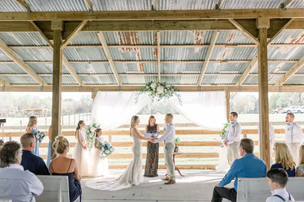 Couple exchanging vows beneath the open-air pavilion with white draping and greenery
