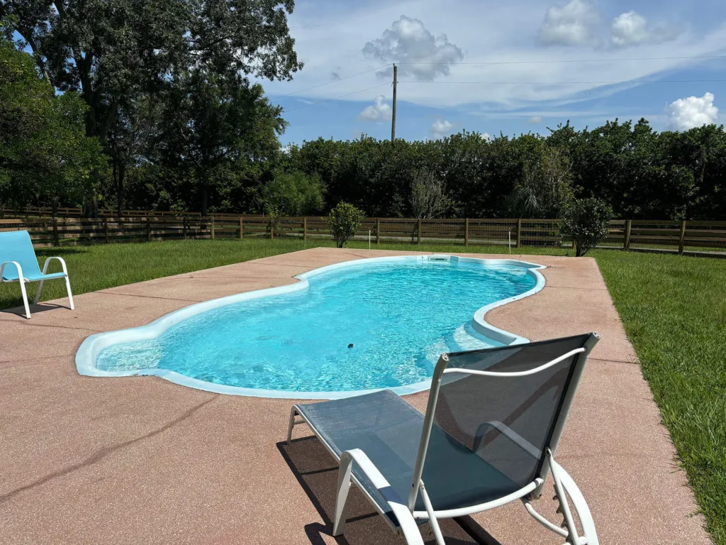 The shared in-ground pool at Triple C Ranch, with lounge chairs on the deck and the pasture fence beyond